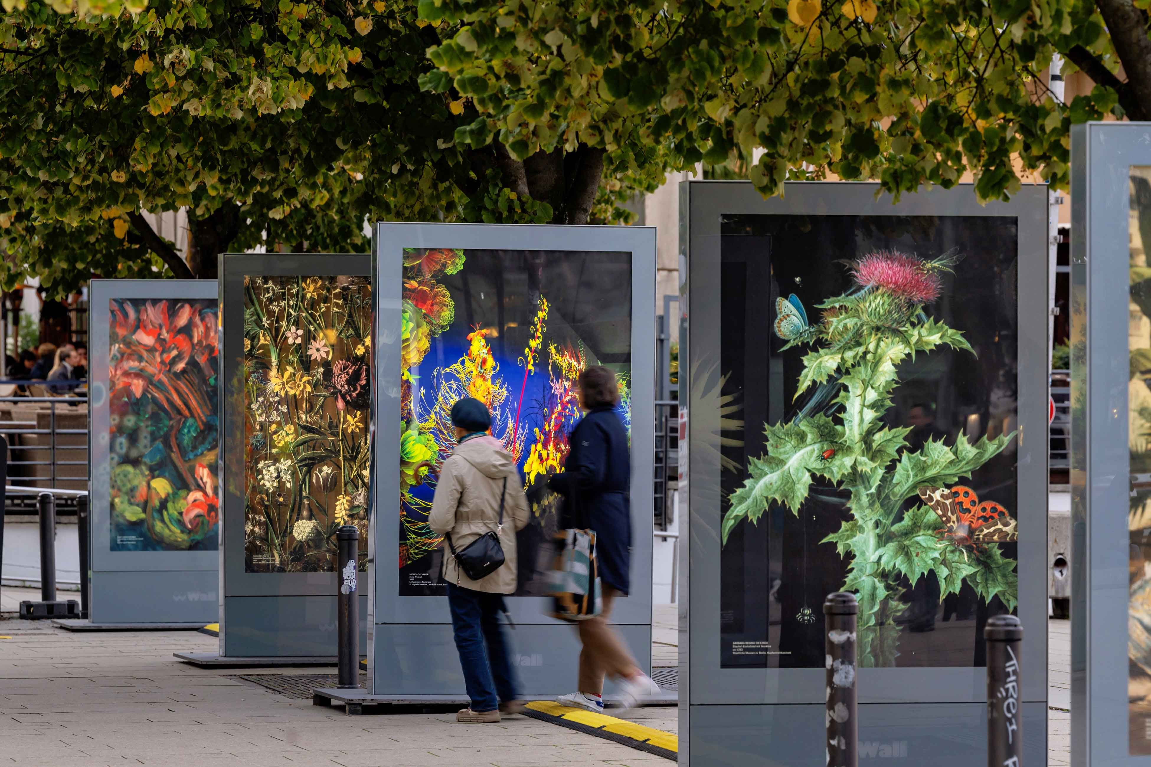 People view vibrant, illuminated digital art pieces displayed outdoors in a public exhibition.